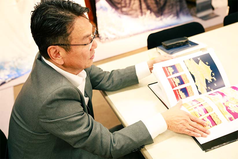 父・和田光正氏の作品集を手に話す、全央社長