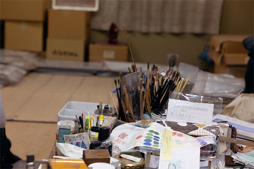 工房の風景。図案作成に使う筆や色見本などが机の上に並べられている